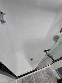White shower with a glass door, drain, and gray floor.