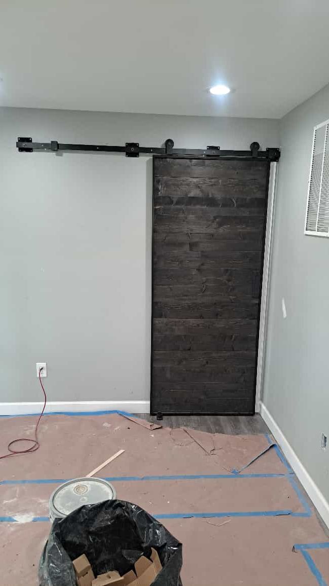 Barn door with black hardware on a gray wall, construction in progress.