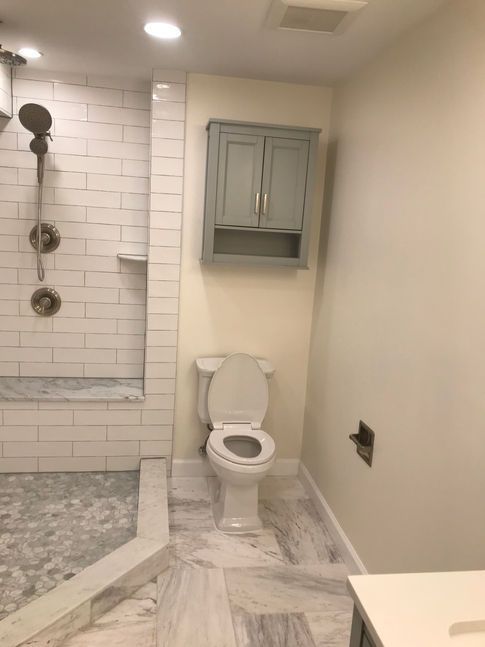 Bathroom with white subway tile shower, toilet, and gray cabinet on a light beige wall.