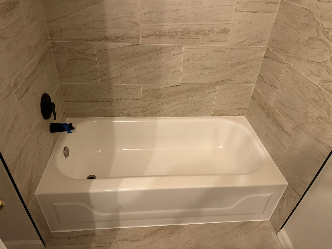 A white bathtub with beige tile walls and a black faucet in a bathroom setting.