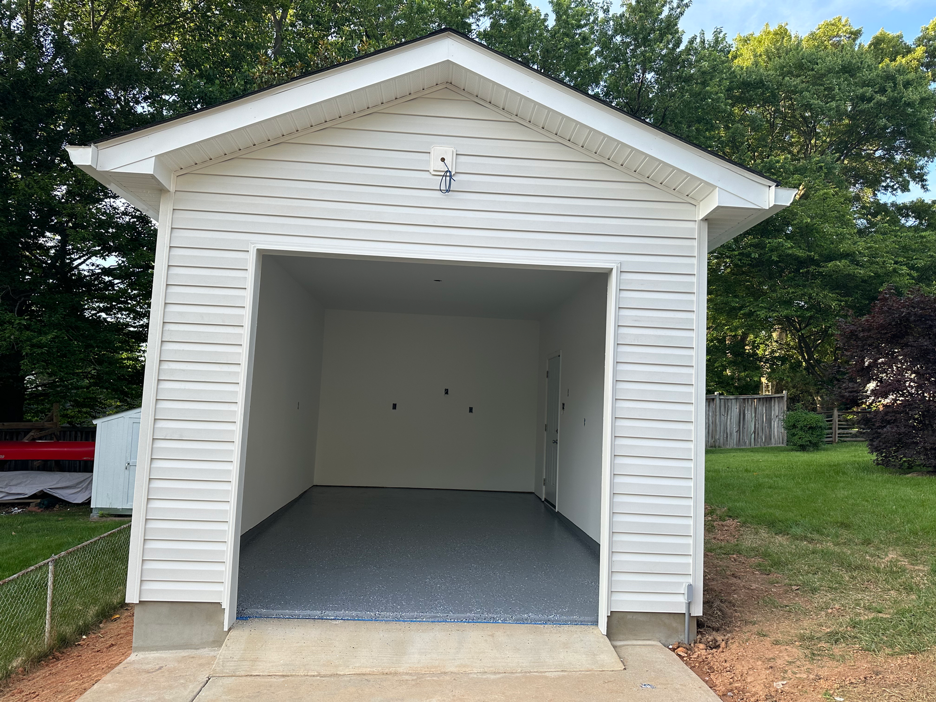 White detached garage with open door, gray speckled floor, and concrete driveway.