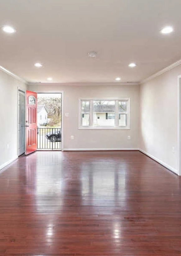 Empty room with red door, hardwood floors, and white walls.