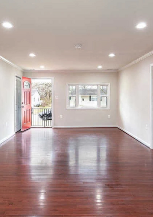 Empty living room with polished wooden floor and open red door.