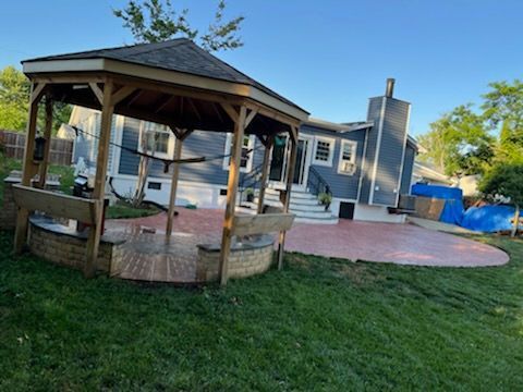 Backyard with gazebo, brick patio, and house. Green grass, blue house, clear sky.