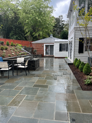 Stone patio with chairs, fire pit, and buildings in a backyard setting. Wet, blue-gray stone.