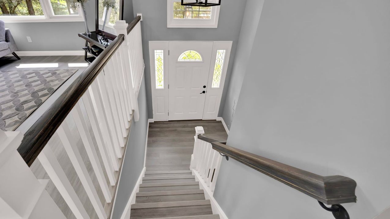 Stairwell leading down to a white front door with glass panels, gray walls, and wood flooring.