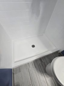 White shower stall with a drain and adjacent toilet.