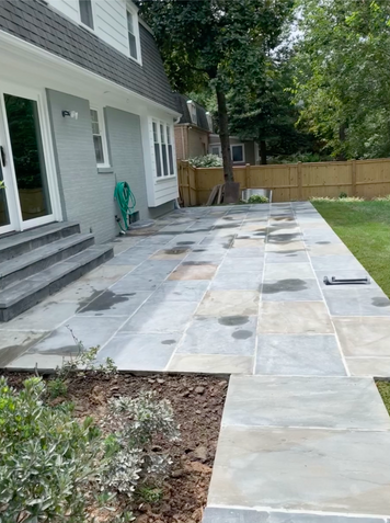 Grey stone patio with a light grey house and grassy yard.