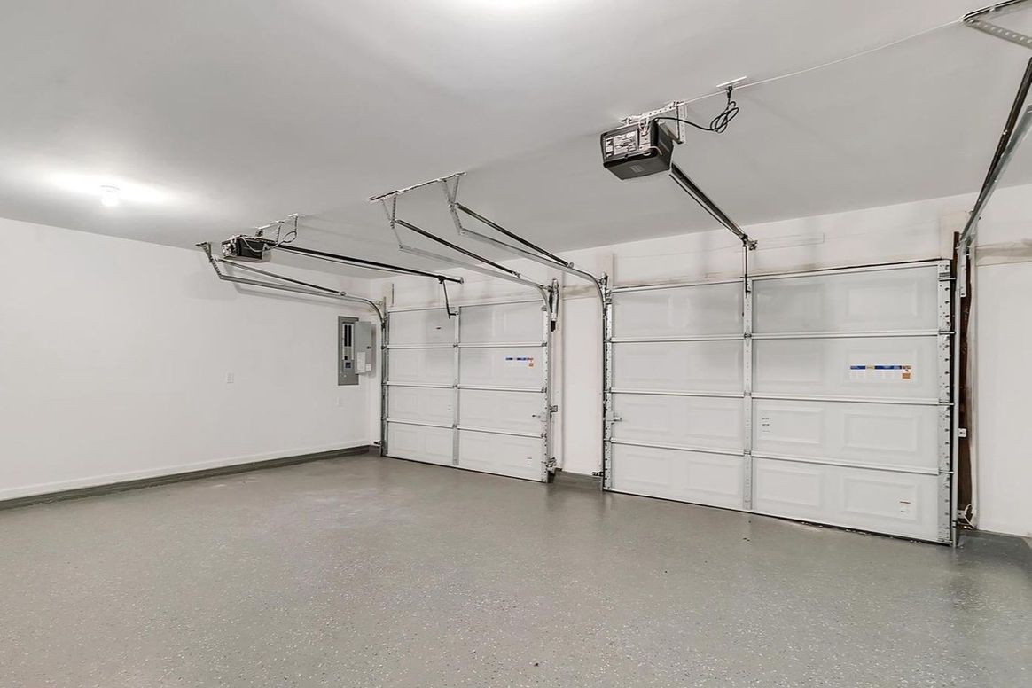 Empty, clean, two-car garage with white walls, gray floor, and two overhead garage doors.