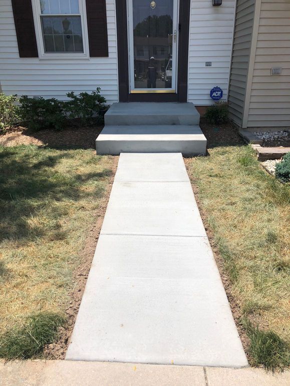 Concrete walkway leading to front door with steps, flanked by grass and landscaping.