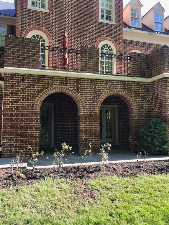 Brick building with arched entryways and a balcony, grassy lawn.