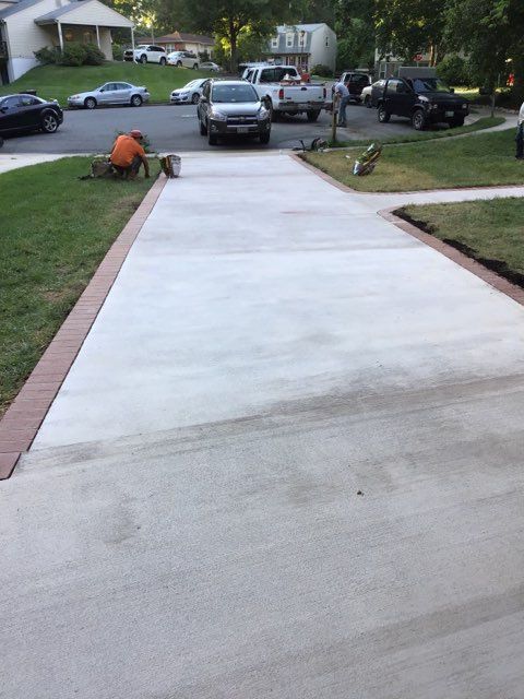 Newly poured concrete driveway with brick border; worker is painting edging.