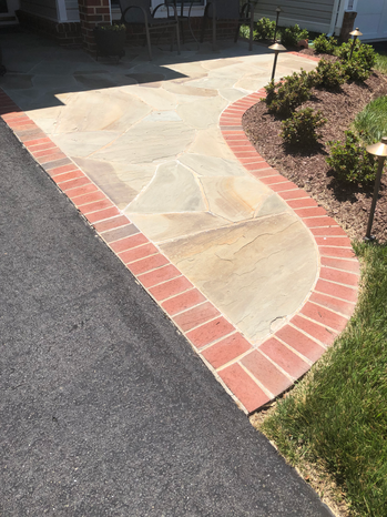 Flagstone walkway with brick edging borders the driveway and garden bed.