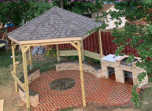 A backyard patio with a gazebo, brick grill, and fire pit on a brick surface.