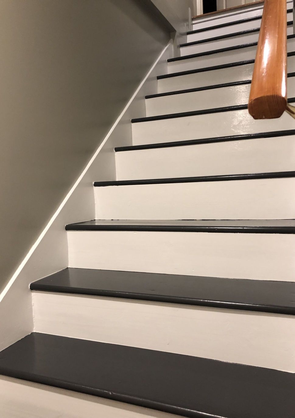 Staircase with white steps, dark grey treads, and a wooden handrail. The wall is light grey.