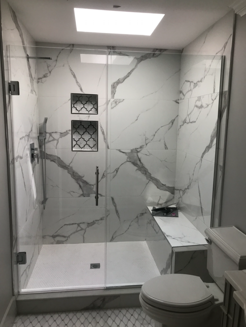 Bathroom with white marble-look tile, glass shower enclosure, built-in bench, and two niches.
