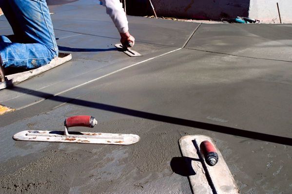 Construction worker smoothing wet concrete with trowels on a sunny day.