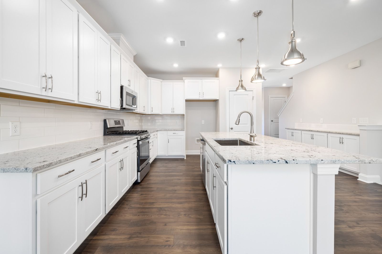 White kitchen with granite countertops, wood floor, and island with sink and hanging lights.