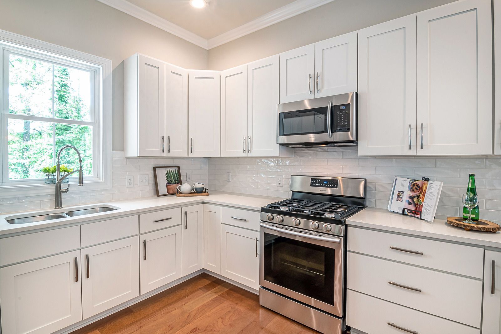 White kitchen with stainless steel appliances and white cabinets, next to a window with outside view.