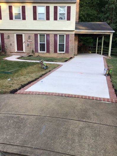 Newly poured concrete driveway with brick border, adjacent to a two-story house with a burgundy door and trim.