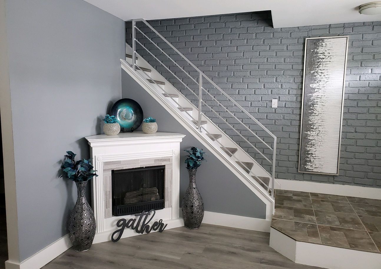 Living room with gray brick wall, white fireplace, stairs, decor.