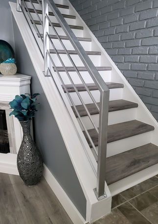 Modern staircase with stainless steel railings, gray treads, white risers, and gray walls.