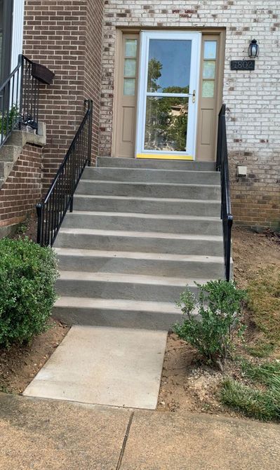 Concrete steps leading up to a front door, flanked by black railings and shrubbery.