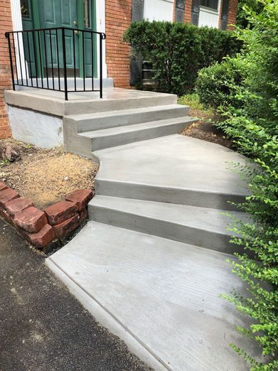Concrete steps leading up to a brick house entrance with black handrail.
