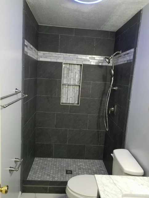 Dark gray tiled shower with a mosaic tile floor, a built-in shelf, and a toilet.