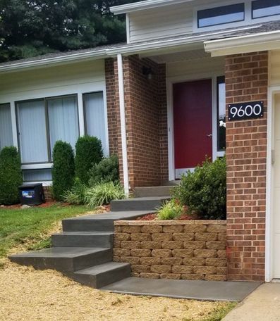 A house entrance with steps and a retaining wall; red door, brick facade, address 9600.