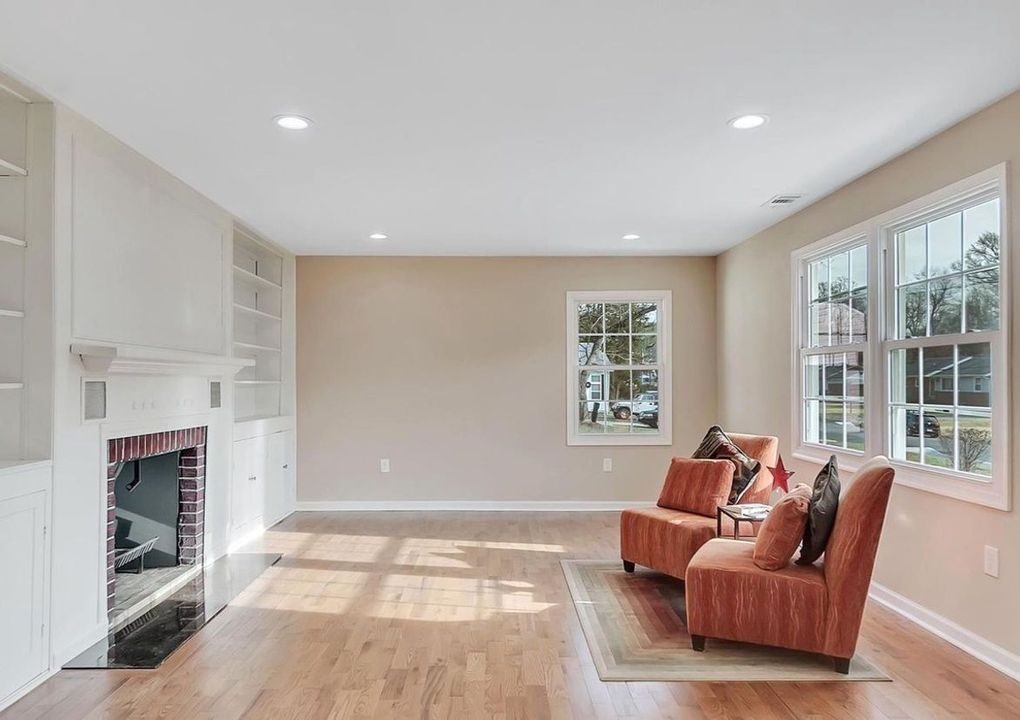 A bright living room with two orange armchairs, a fireplace, and large windows.