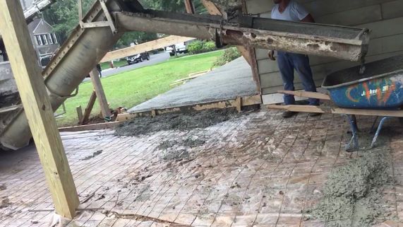 Concrete being poured over a brick patio from a truck with a man directing the flow.