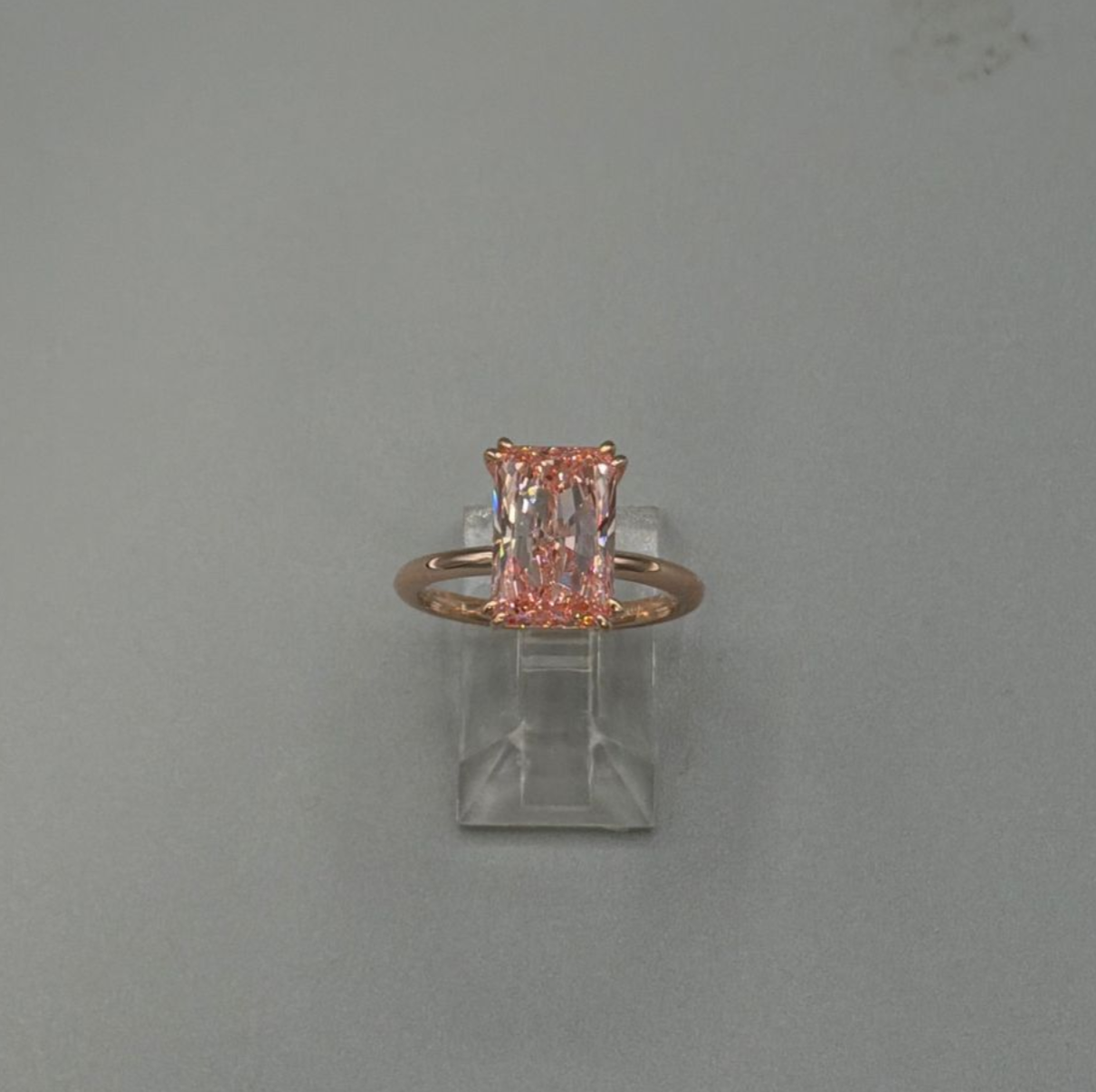 Small clear glass jar with a copper ring and pink decorative piece on top against a gray background