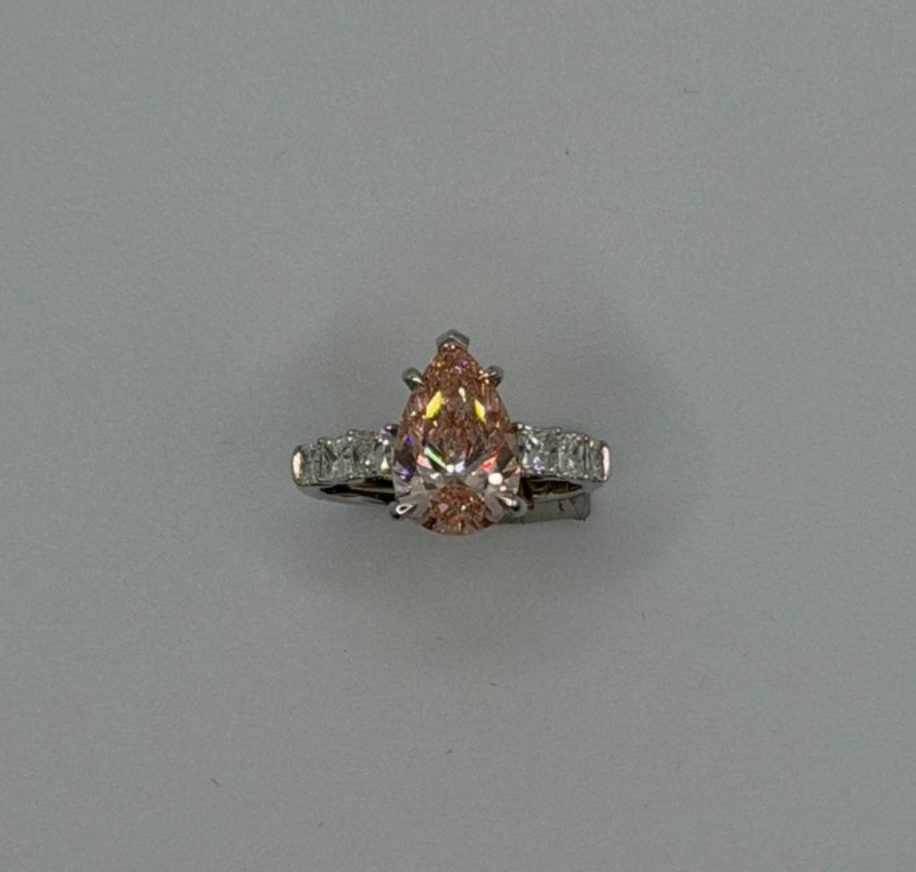 Pink pear-cut gemstone ring with silver band and small side stones on a plain gray background