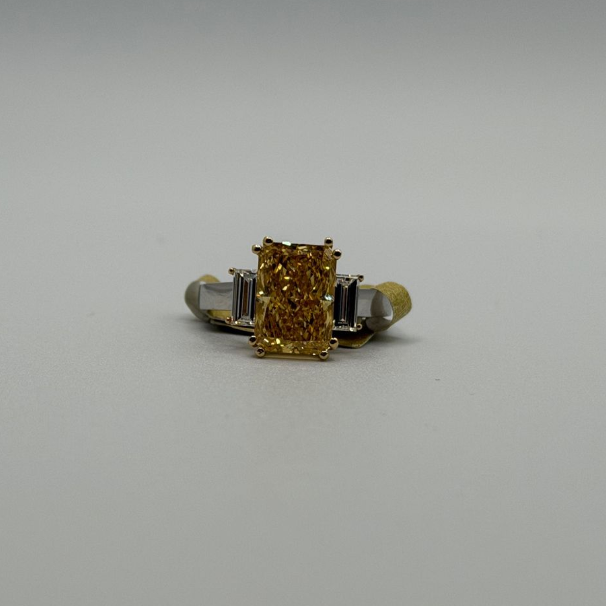 Gold ring with a rectangular yellow center stone and side accents on a plain white background
