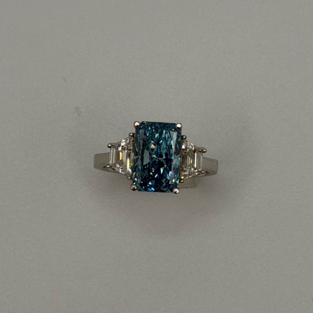 Silver ring with a rectangular blue gemstone and small side stones on a gray background