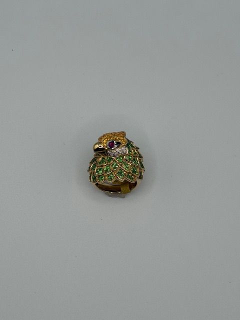 Small jeweled owl-shaped brooch with green, purple, and gold details on a gray background
