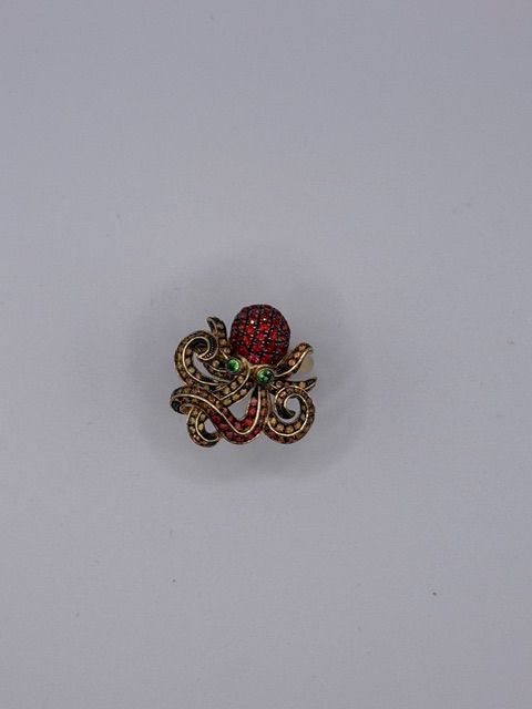 Small jeweled brooch with red, green, and gold stones on a plain light background