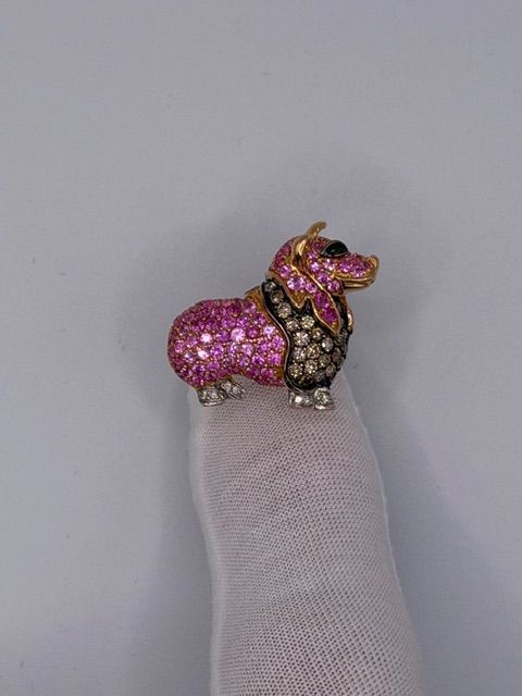 Pink jeweled dog figurine sitting on a gloved finger against a plain background