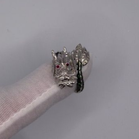 Silver cat ring with red eyes and a dangling black teardrop charm on a white textured surface