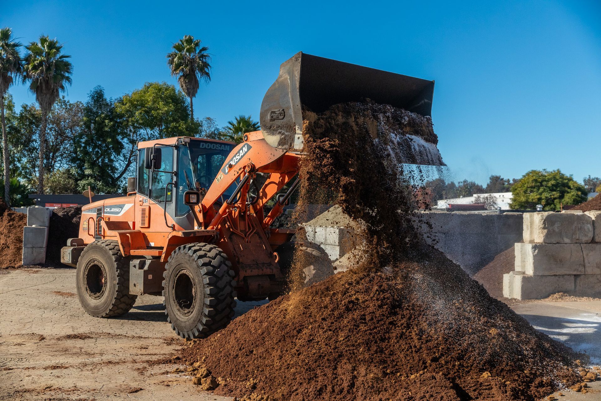 Orange front-end loader dumping mulch on a sunny day.