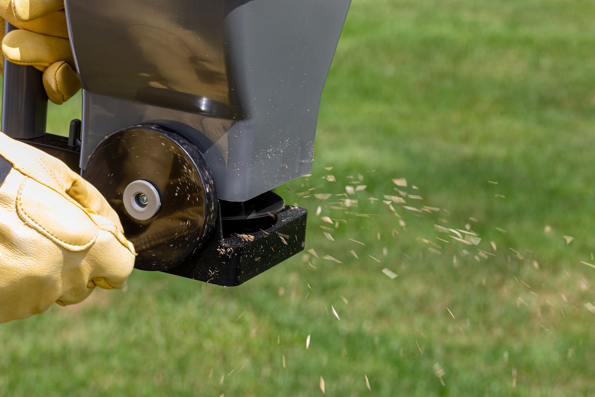 A person in gloves uses a spreader to distribute granular material on a green lawn.