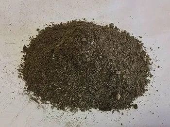 Pile of dark, granular soil on a light-colored surface.