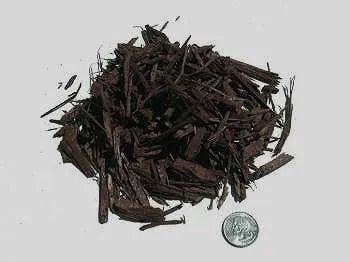 Pile of dark brown mulch next to a quarter coin, on a white surface.