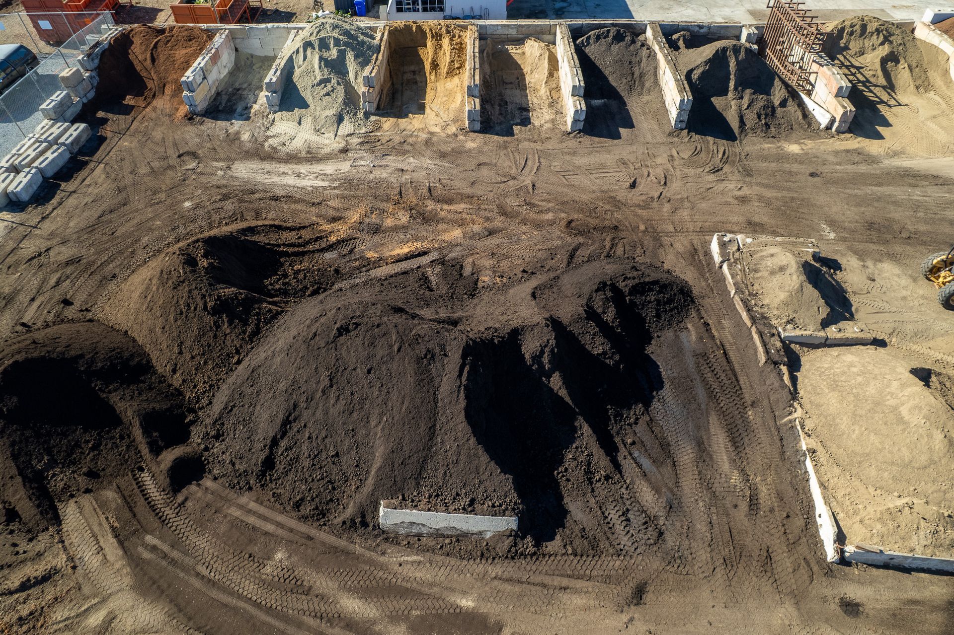 Overhead view of a materials yard with piles of soil and materials stored in concrete bays.
