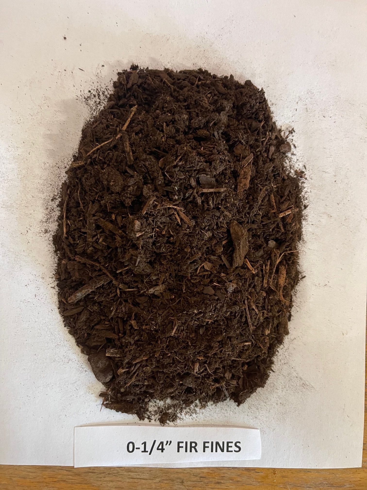 Pile of dark brown fir fines on white paper; labeled