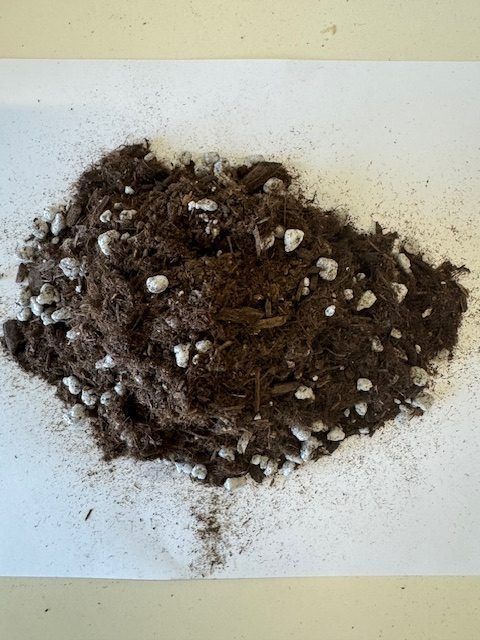 Pile of dark brown soil mixed with white perlite, on white paper.