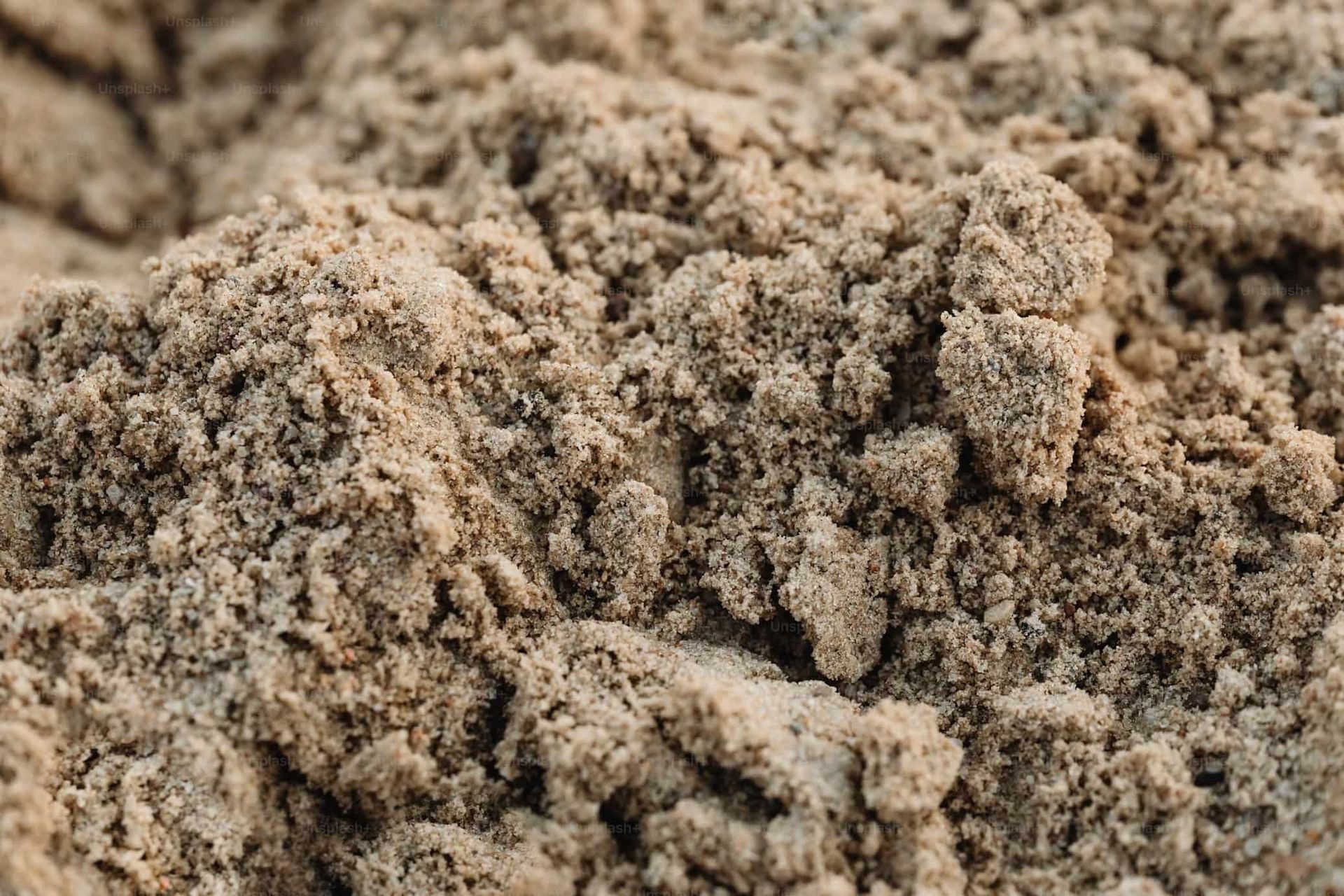 Close-up of light brown, grainy sand with rough, textured surface.