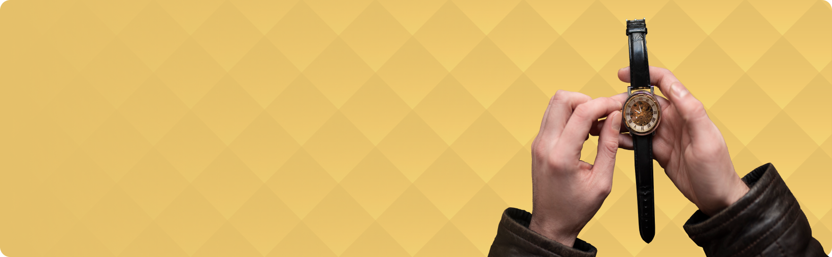 A person is holding a watch in their hands on a yellow background.