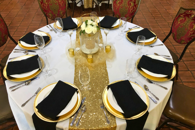A large event hall with round tables set for guests, beige walls, and brown chairs.